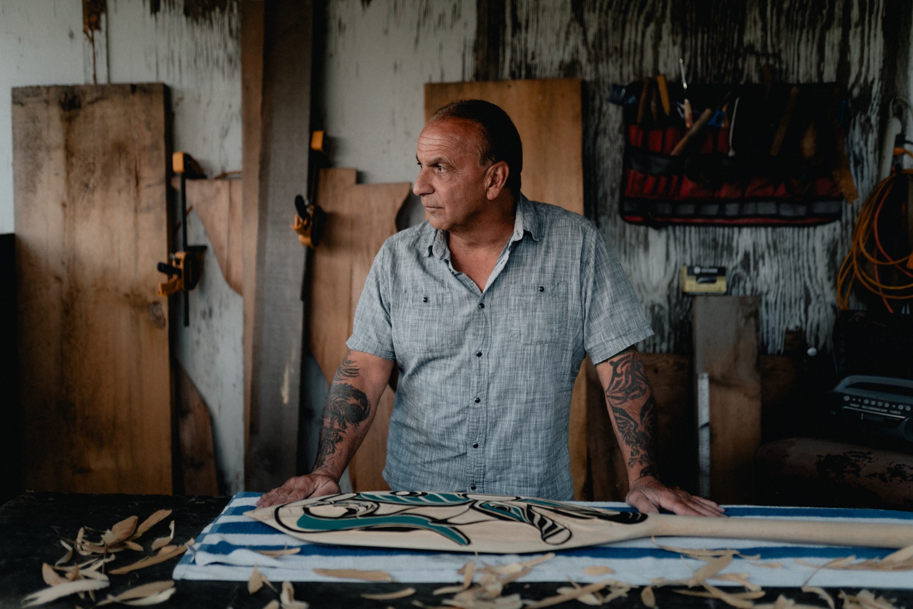 A carver at his workbench with a carved and painted paddle
